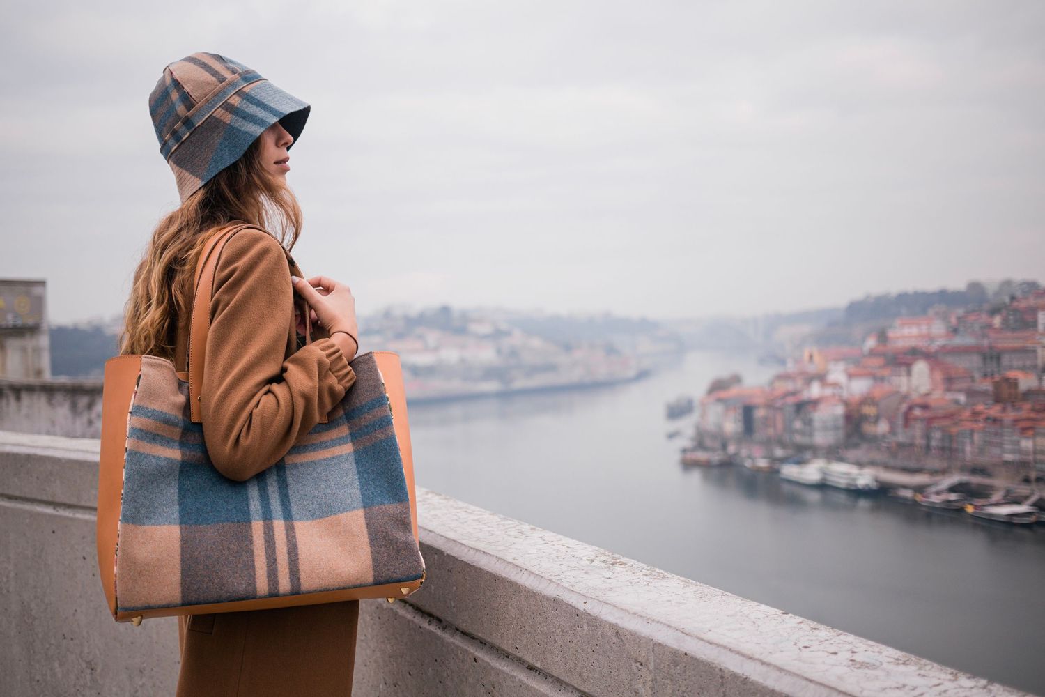 A person wearing winter attire gazes at Porto's cityscape and Douro River from a scenic overlook on a foggy day.