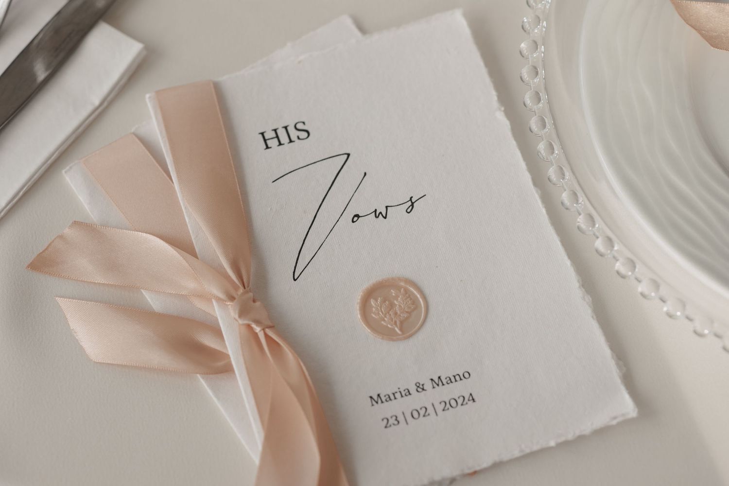 Wedding invitation card with blush pink ribbon and wax seal on white paper featuring elegant 'His Vows' text.