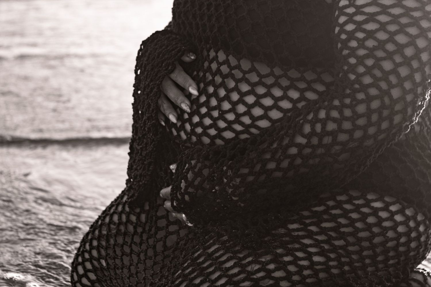 Expecting Mexican mother on the beach in Brookings in a black swimsuit and a black crochet coverup, caressing her belly