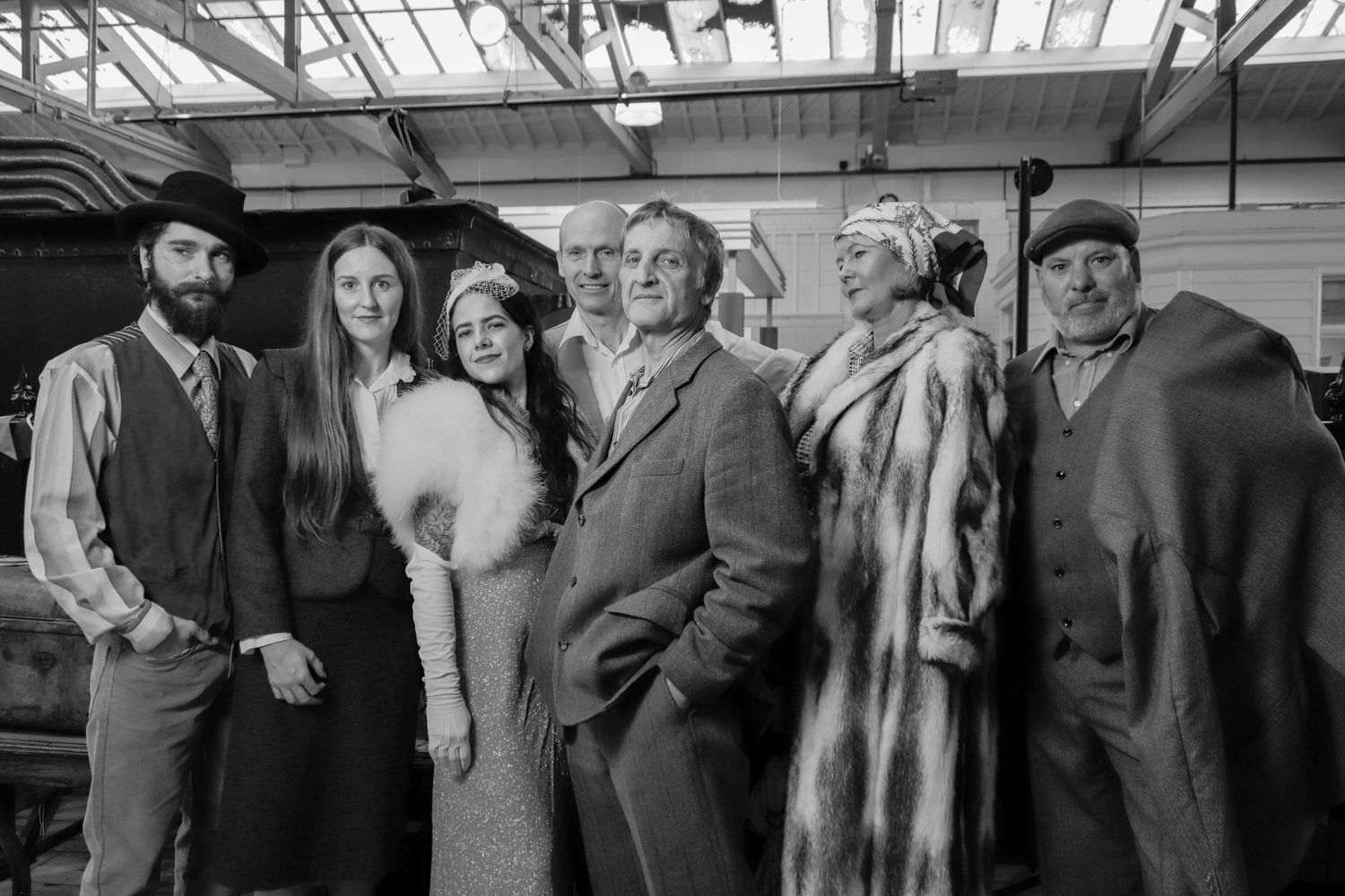 Vintage style group photo of people in formal attire inside conservatory.