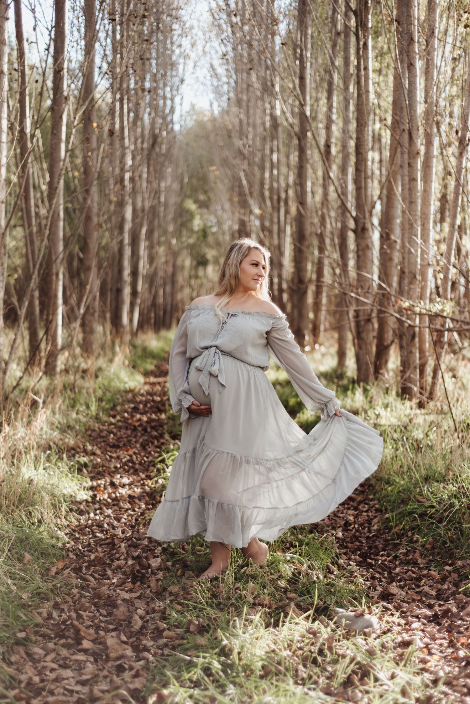 Maternity photo of woman twirling in flowy gray dress among birch trees.