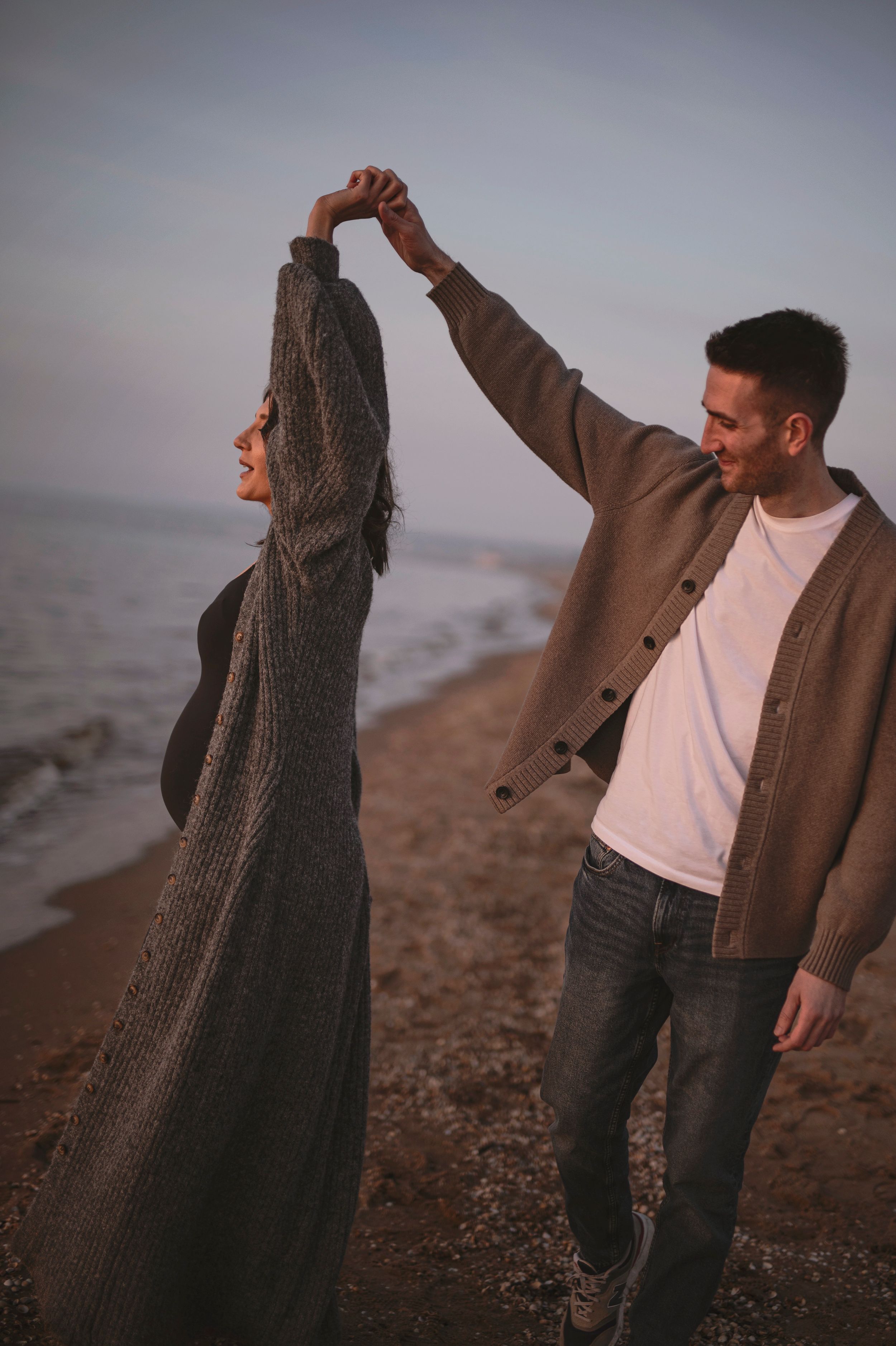 Couple dancing and twirling together at sunset on a rocky beach shore with moody lighting.