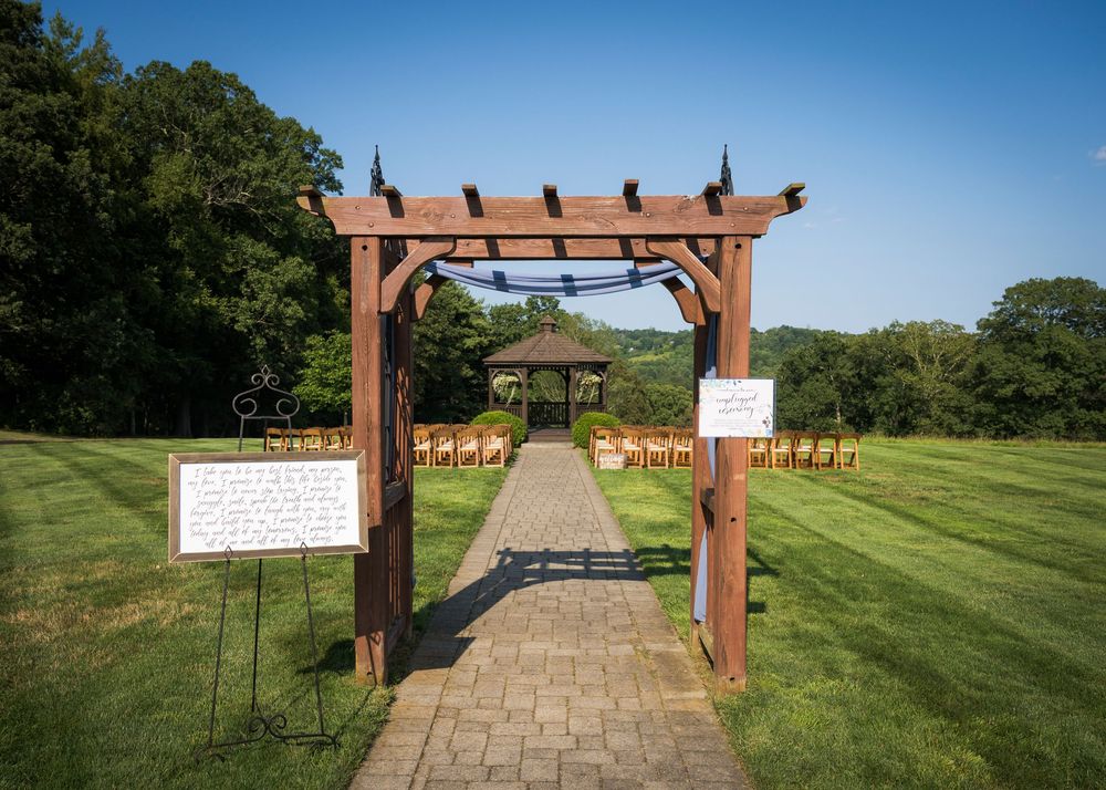 Outdoor wedding ceremony venue with wooden arch and rows of white chairs on stone path.