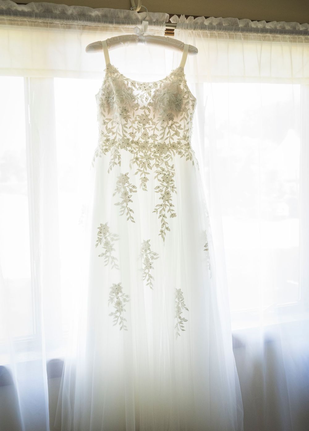 White wedding dresses hanging in a row against sheer curtained windows.