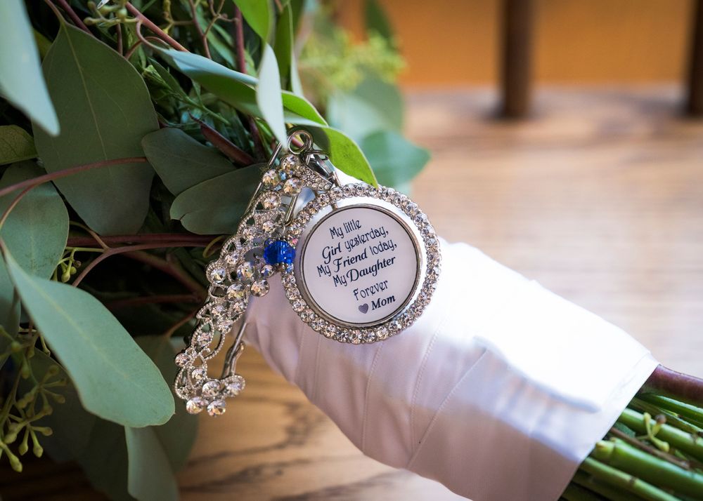 Hands in white gloves hold delicate eucalyptus branches with sparkling jewelry details against a warm wooden backdrop.