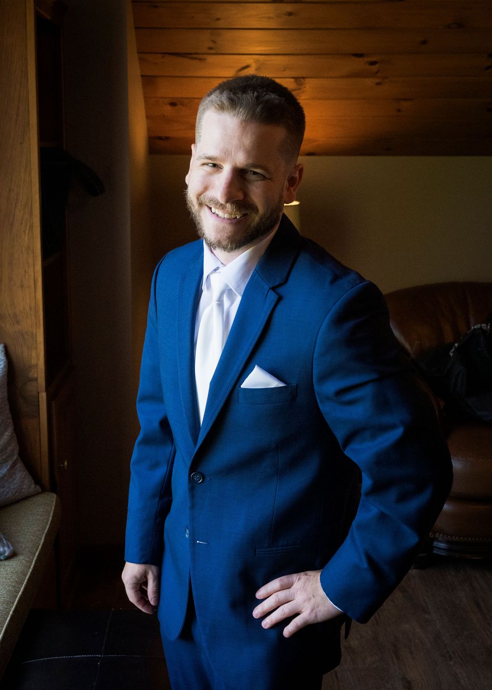Wedding party member in a navy blue suit poses in rustic wooden interior.