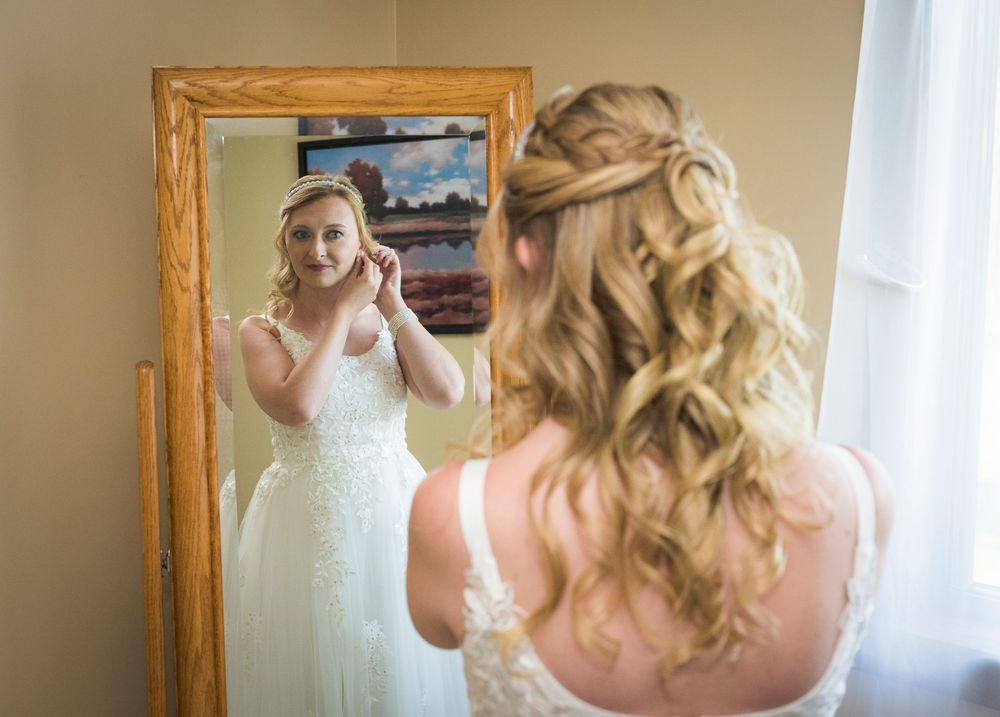 Getting ready scene with bridal gown reflected in framed mirror.