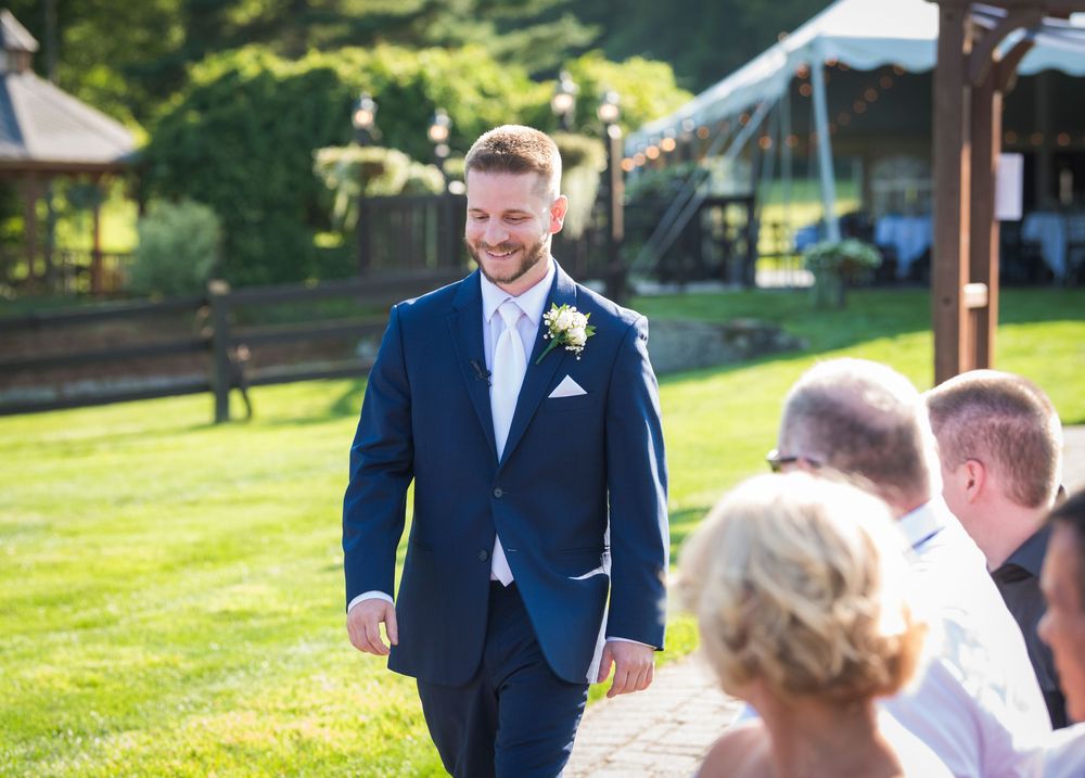 Outdoor wedding party posing on a sunny green lawn wearing navy blue suits and light colored dresses.