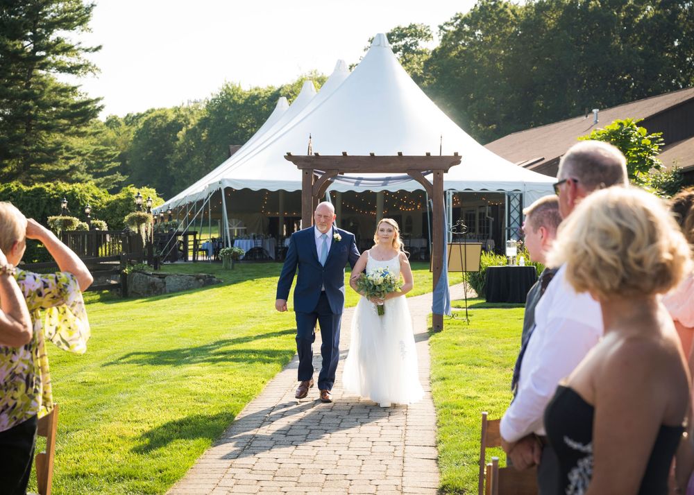 Outdoor wedding ceremony setup with white tent and stone pathway in a green garden setting.