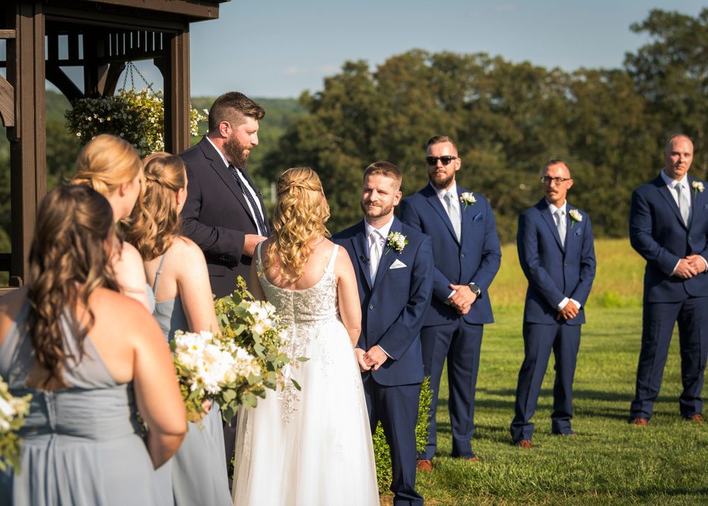 Wedding party in navy and grey attire poses outdoors on sunny day.