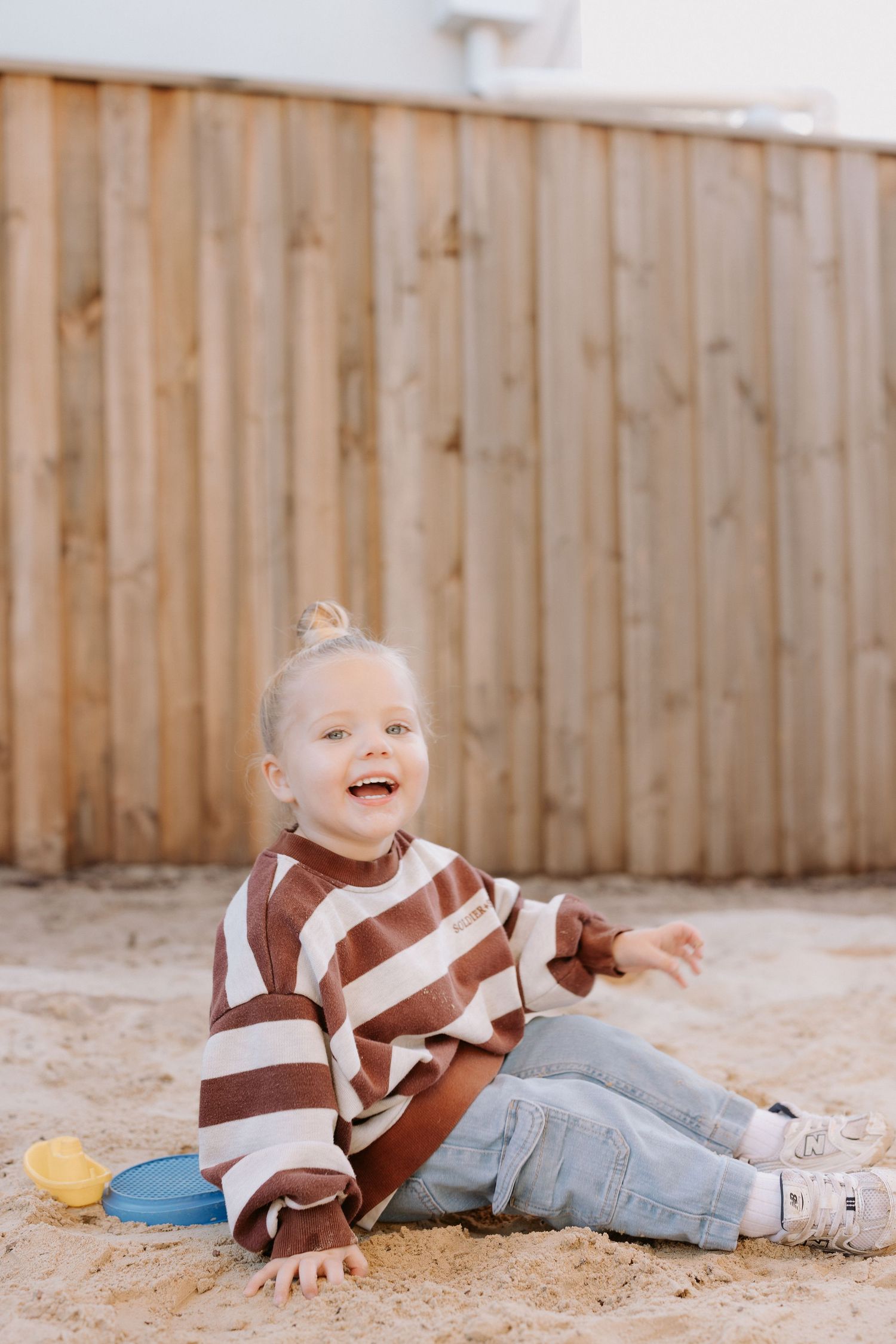 Smiling toddler in beige shirt sitting at table indoors.