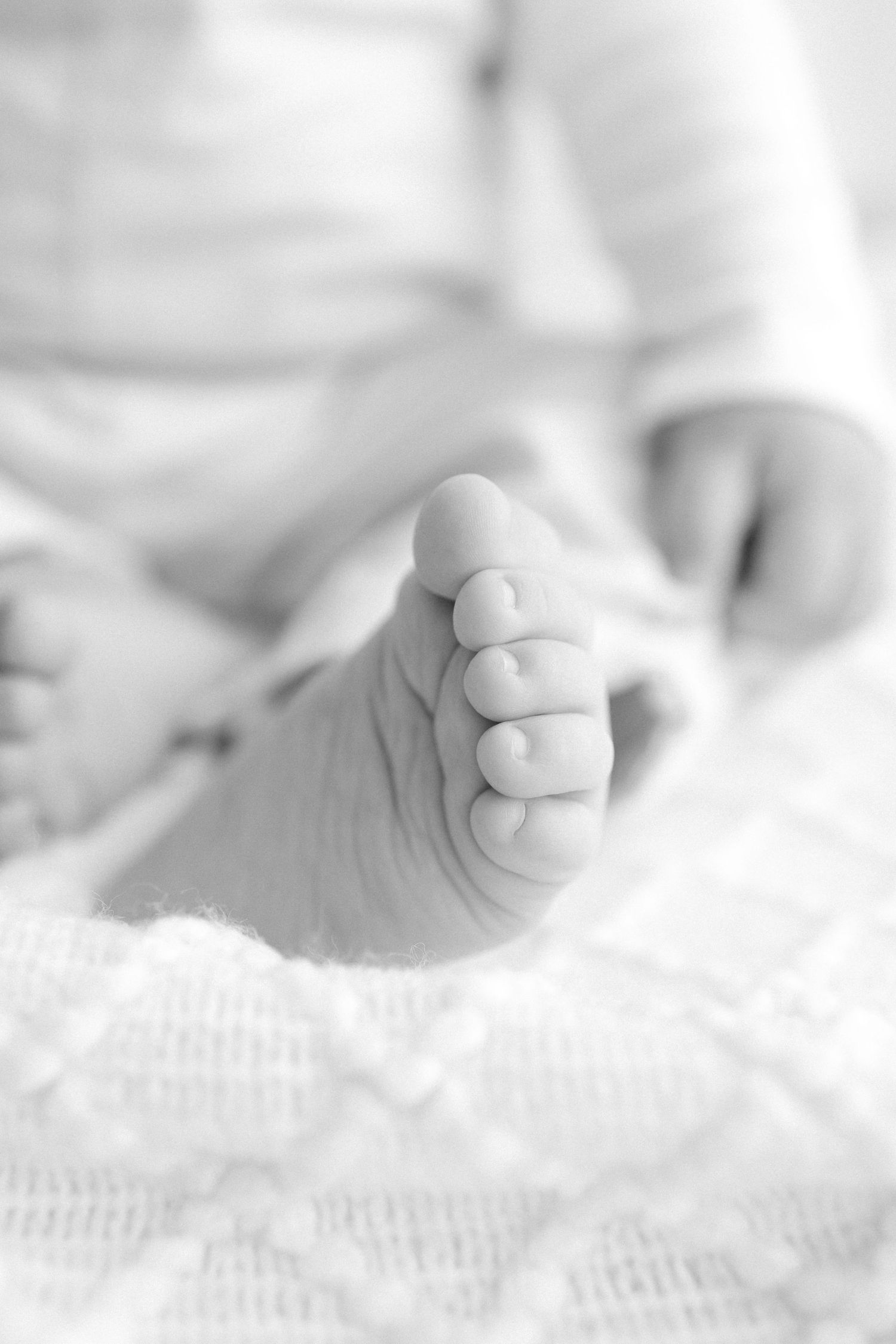 Black and white close-up photo of a newborn baby's tiny foot resting on a soft white blanket.