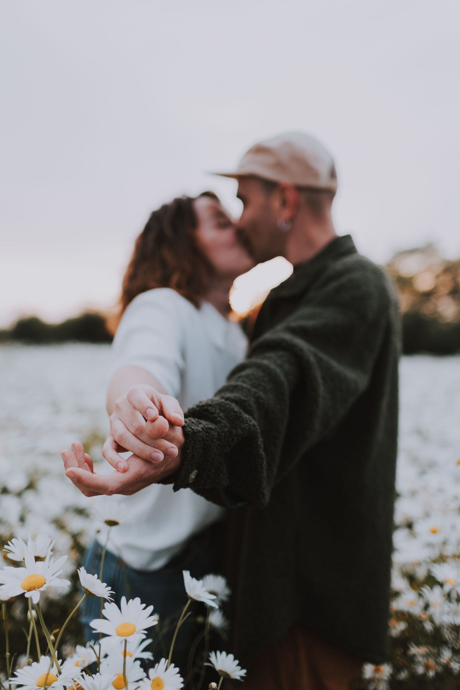 Couple embracing in daisy field during golden hour.
