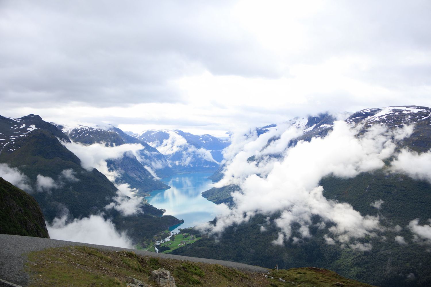 Dramatic view of Norwegian fjord through clouds with snow-capped mountains in background.