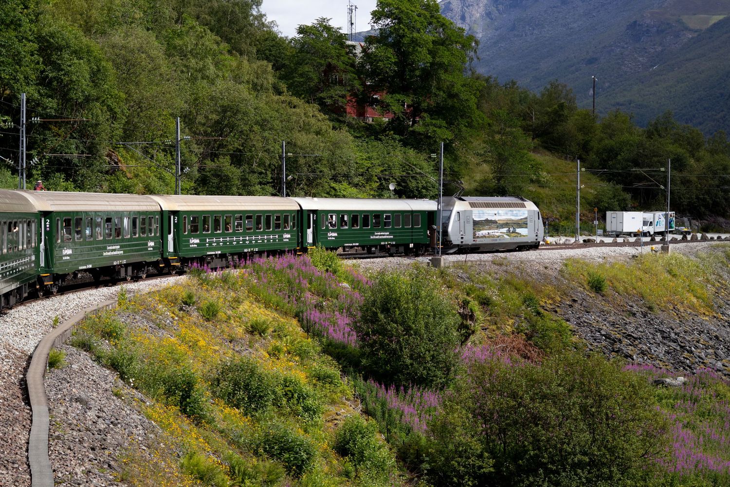 Vintage green train cars winding through mountainous terrain with caravans alongside.