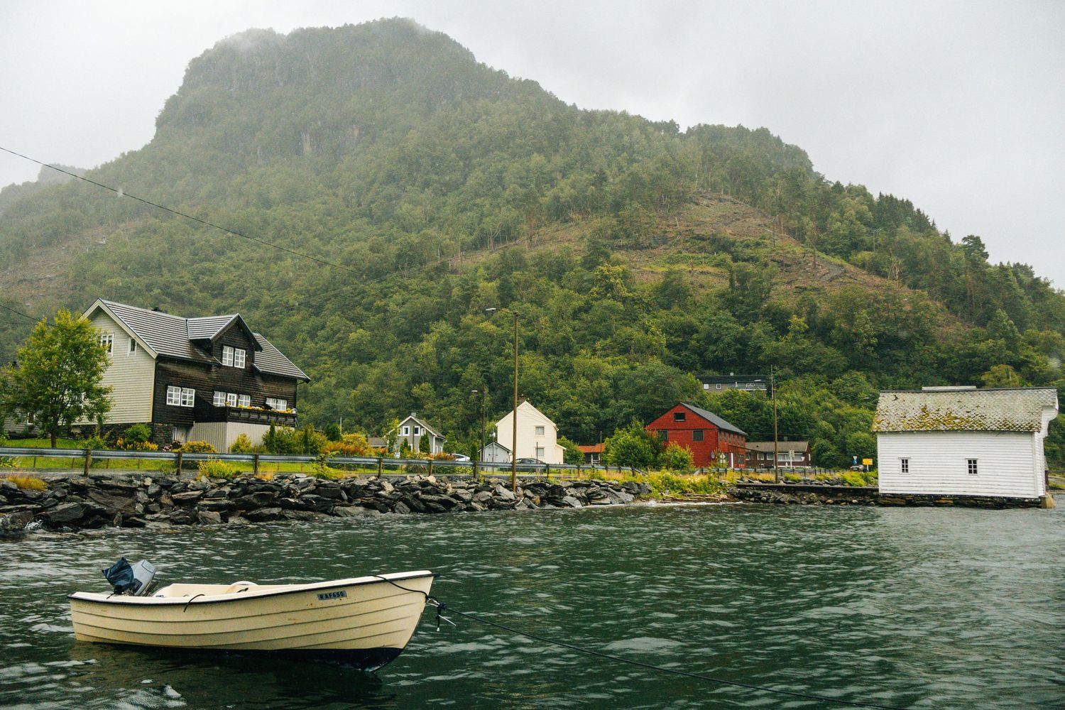 Colorful wooden houses line the shore of a Norwegian fjord with a small boat in the foreground.