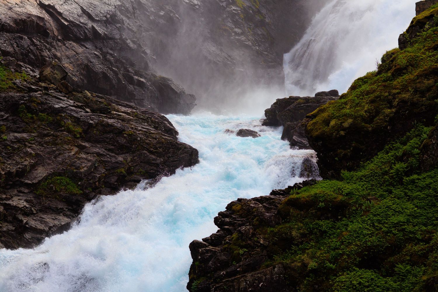 Dramatic waterfall rushing through rocky cliffs with turquoise water and moss-covered stones.