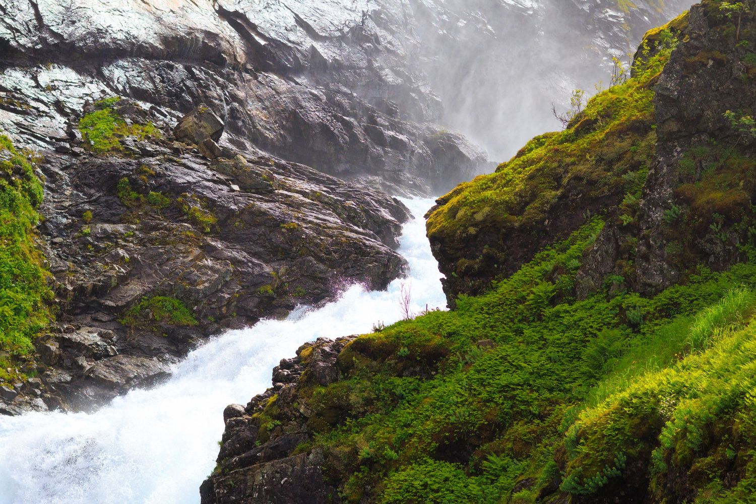 Cascading waterfall flowing down steep rocky cliffs surrounded by green vegetation.