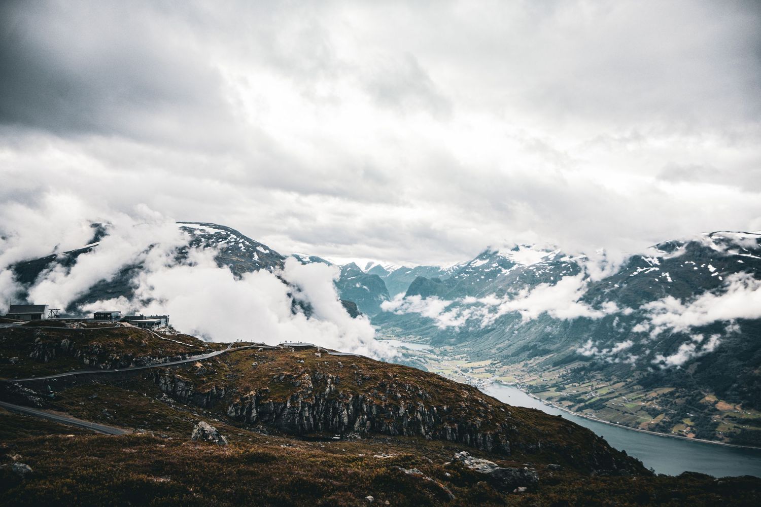 Rocky mountain landscape with snow-covered peaks and cloudy skies in Norwegian fjord region.