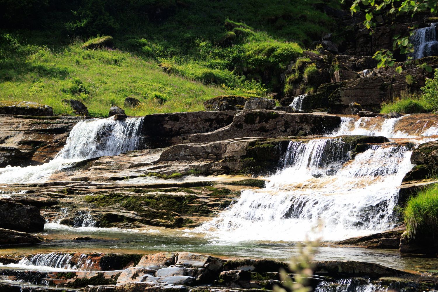 Cascading waterfall flows over rocky ledges in a sunlit natural setting.