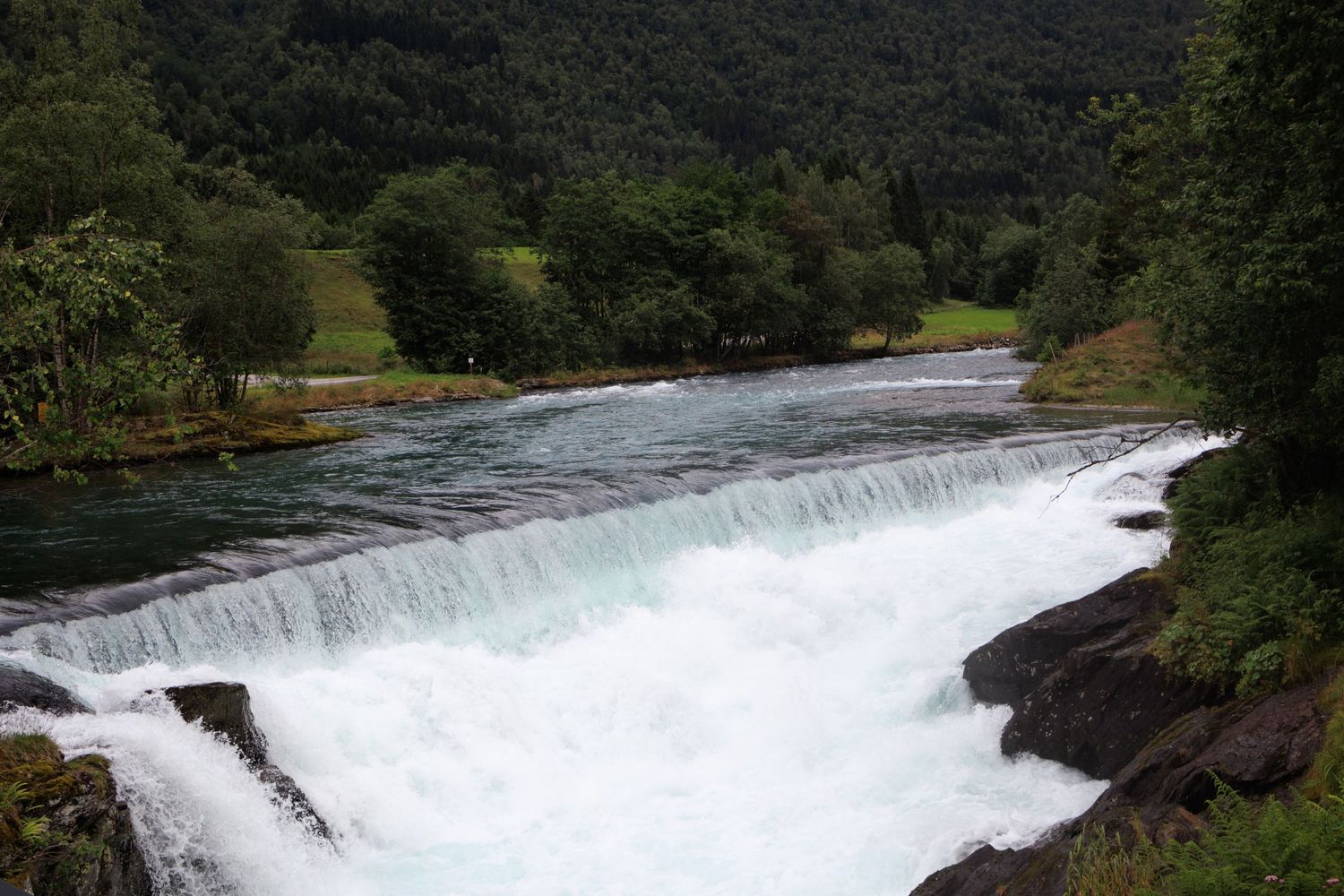 Powerful waterfall cascading over rocks in a lush green mountain setting.