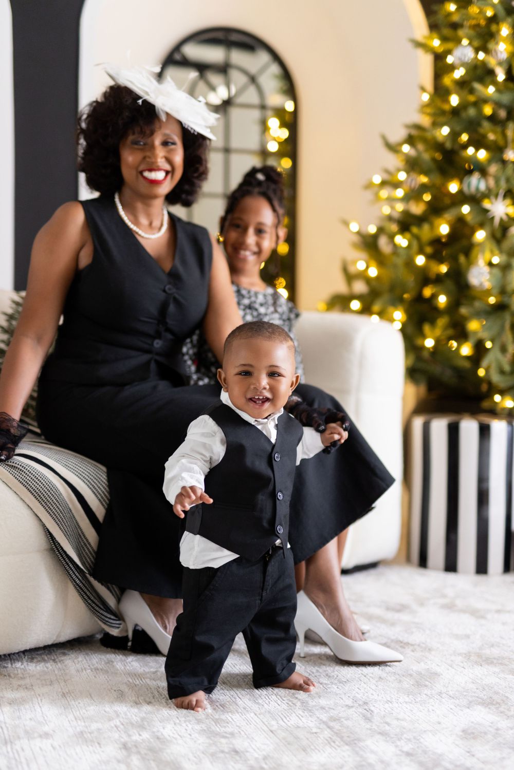 A family poses together in elegant formalwear by a decorated Christmas tree in a bright, festive interior setting.