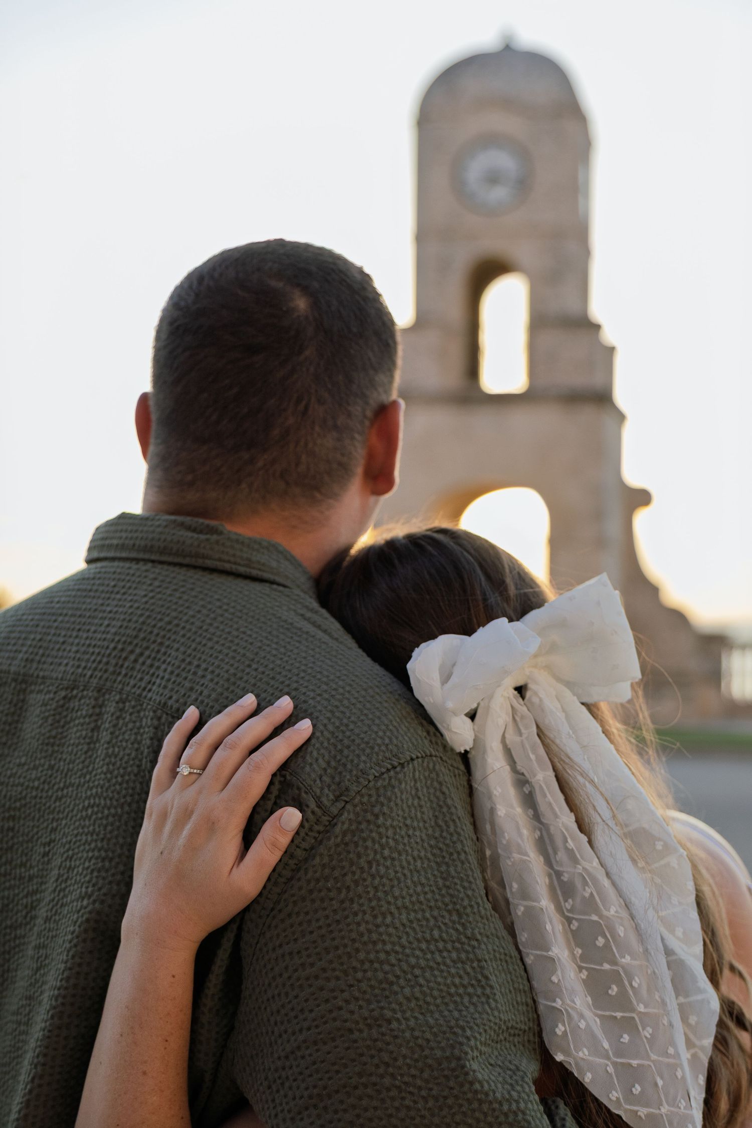 Couple embracing near church bell tower at sunset.