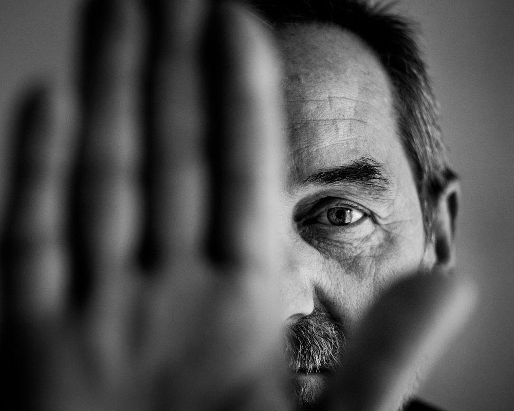 Black and white artistic portrait showing half a face with a raised palm blocking the other half in dramatic lighting.