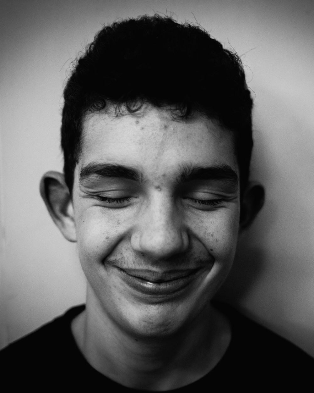 Black and white portrait photo of someone with eyes closed smiling warmly against a neutral background.