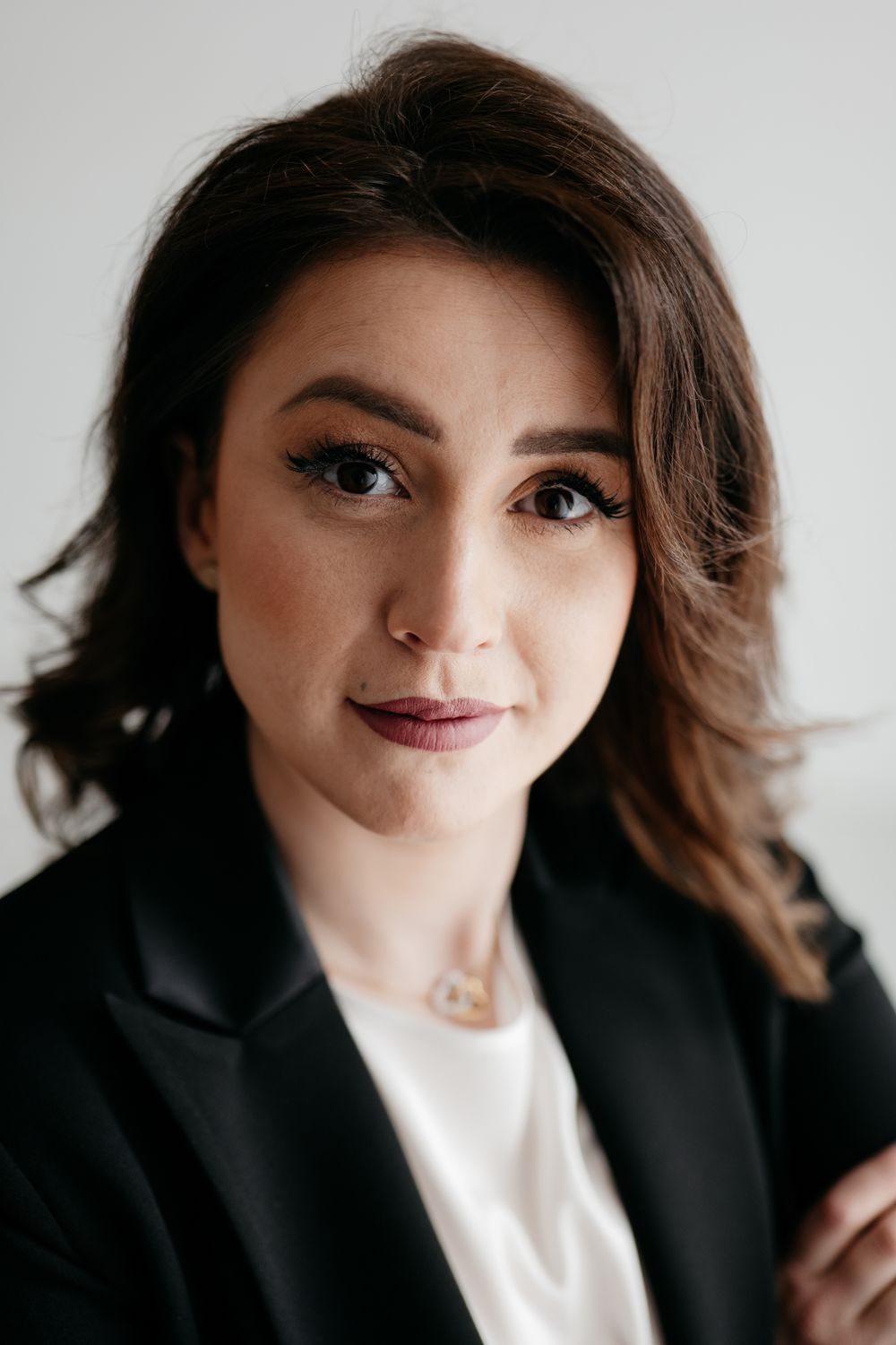 Professional studio portrait of a woman in black blazer and white top against light background.