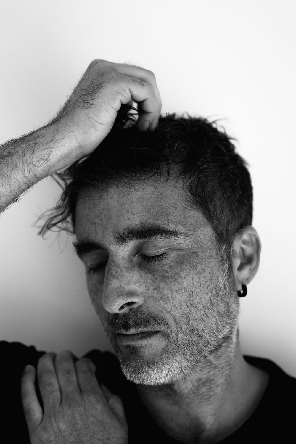 Black and white portrait showing closed eyes and hand gestures expressing contemplation or distress.