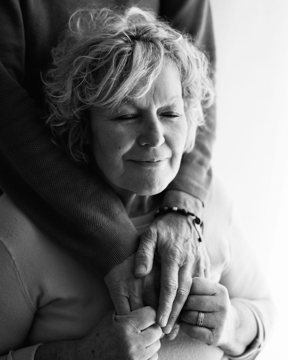 Black and white portrait of someone holding hands in a tender moment smiling with eyes closed and curly hair.