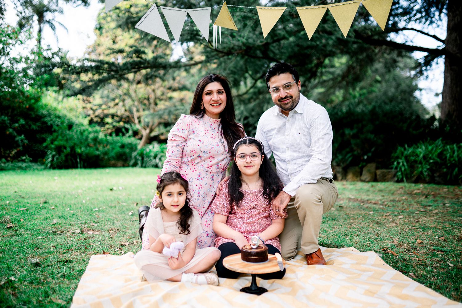 A happy family of 4 in Melbourne's St Kilda Botanical Gardens with lush greeneries as backdrop taken by a Melbourne family photographer.