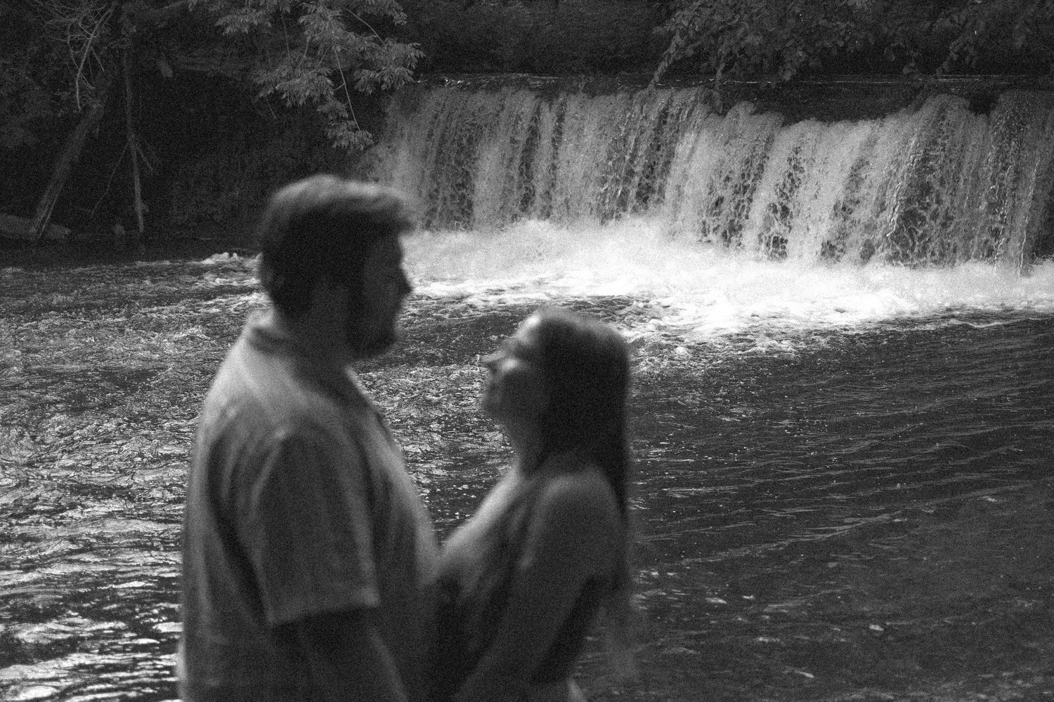 A couple stands in silhouette by a cascading waterfall, creating a romantic black and white scene.