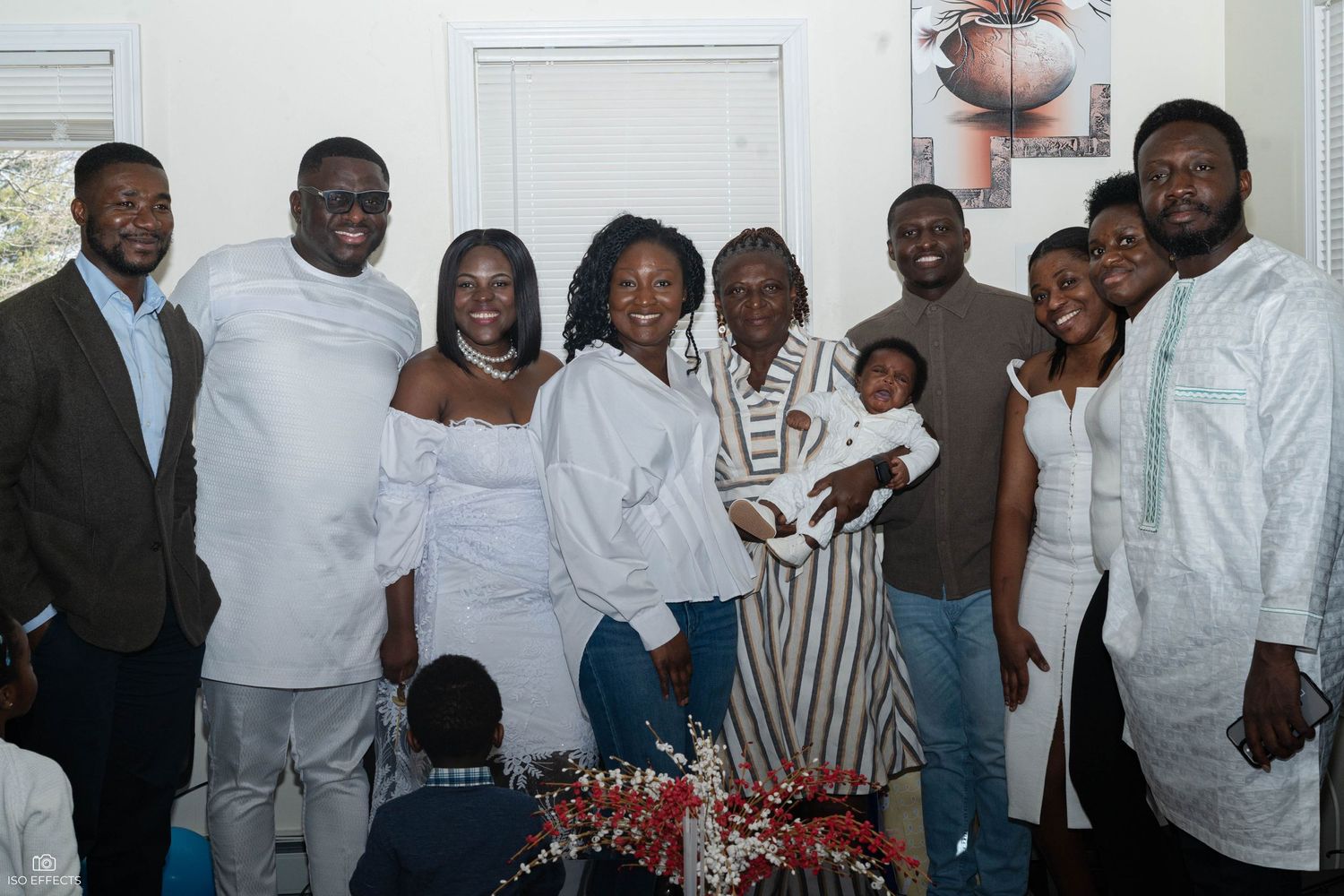 A group dressed in white and cream colored clothing poses together at an indoor gathering.