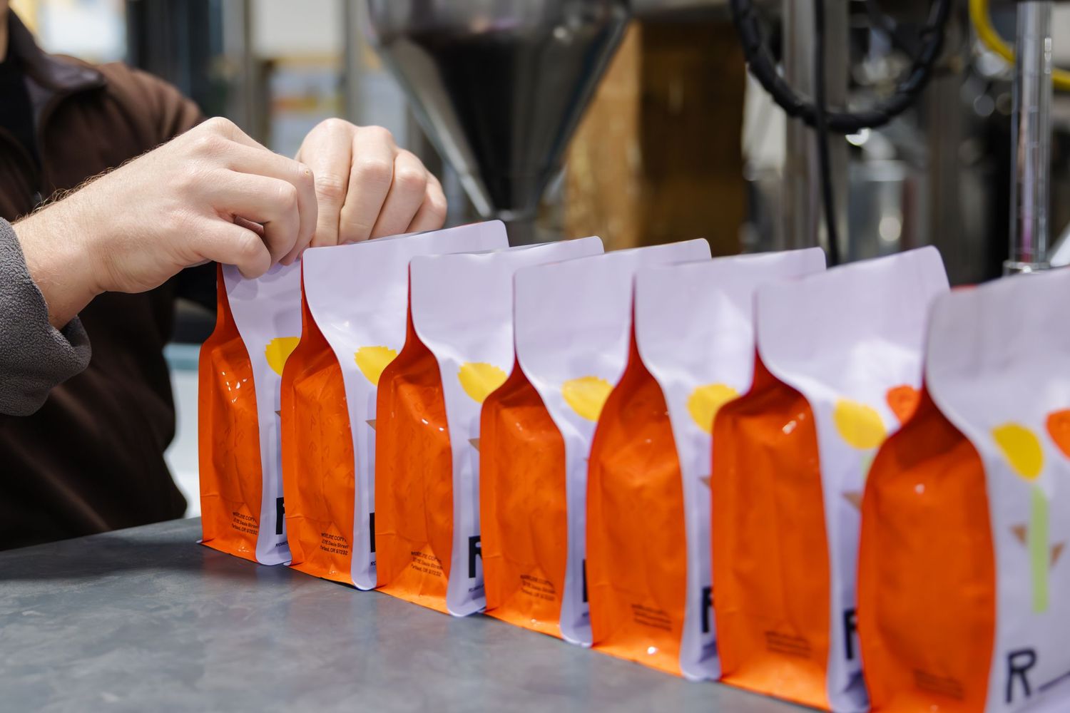 Orange paper bags lined up in a row being prepared on a table during a craft or packaging activity.