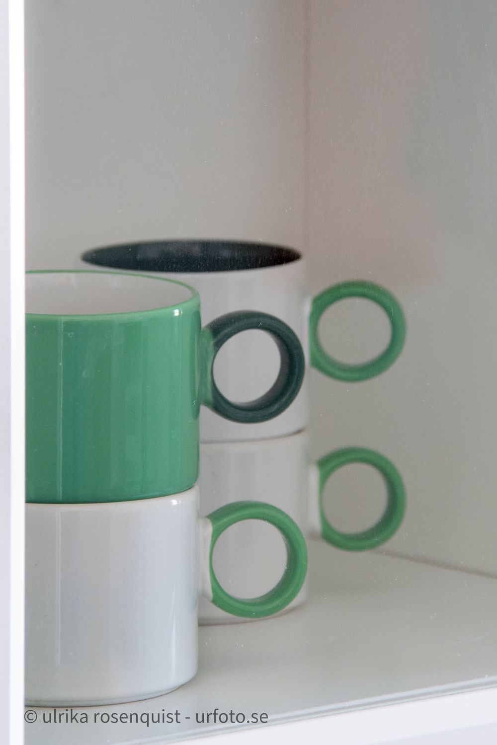Green and white stacked coffee mugs with circular handles displayed on white shelf.
