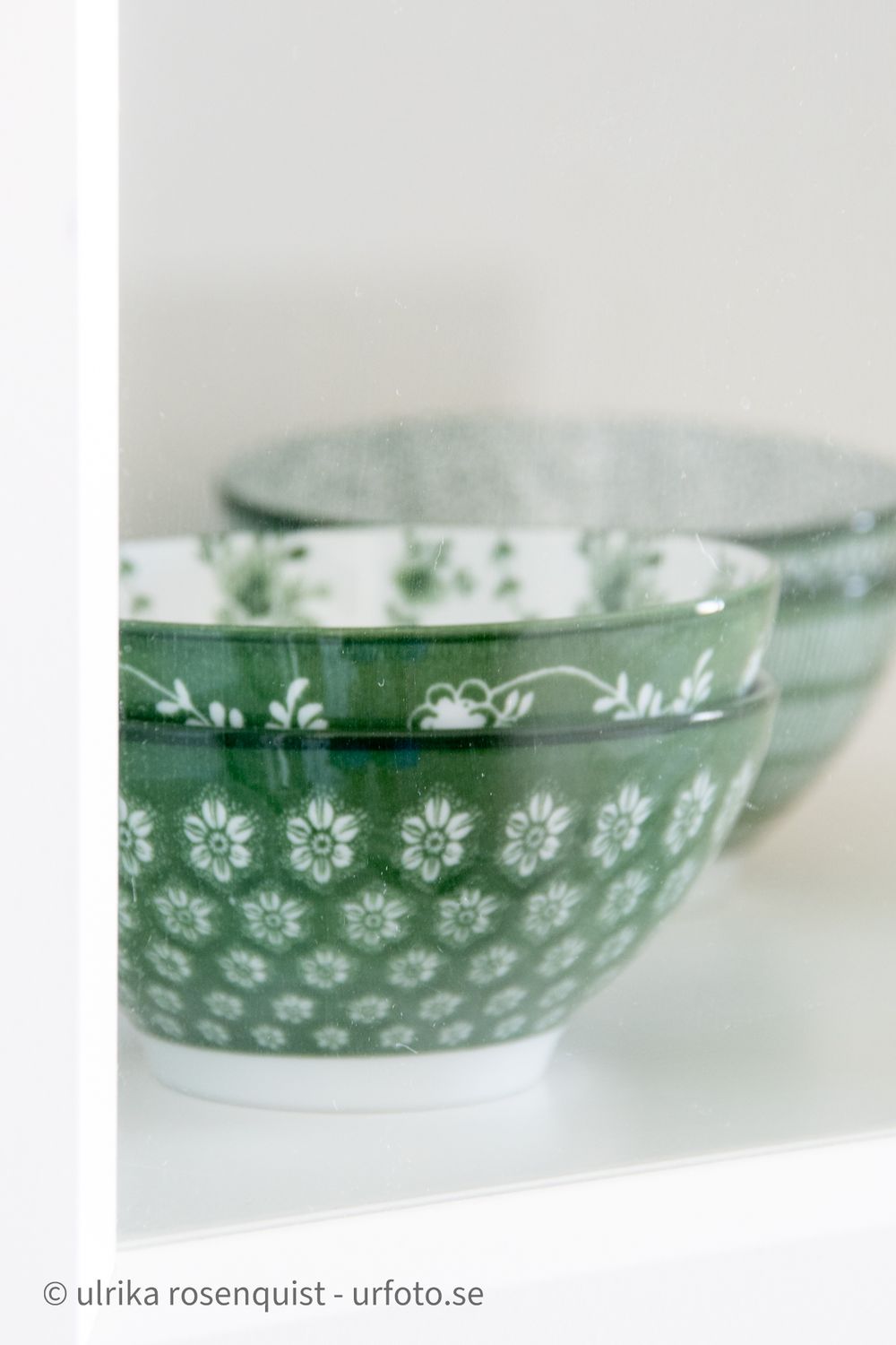 Green ceramic bowls with delicate white floral patterns photographed against light background.