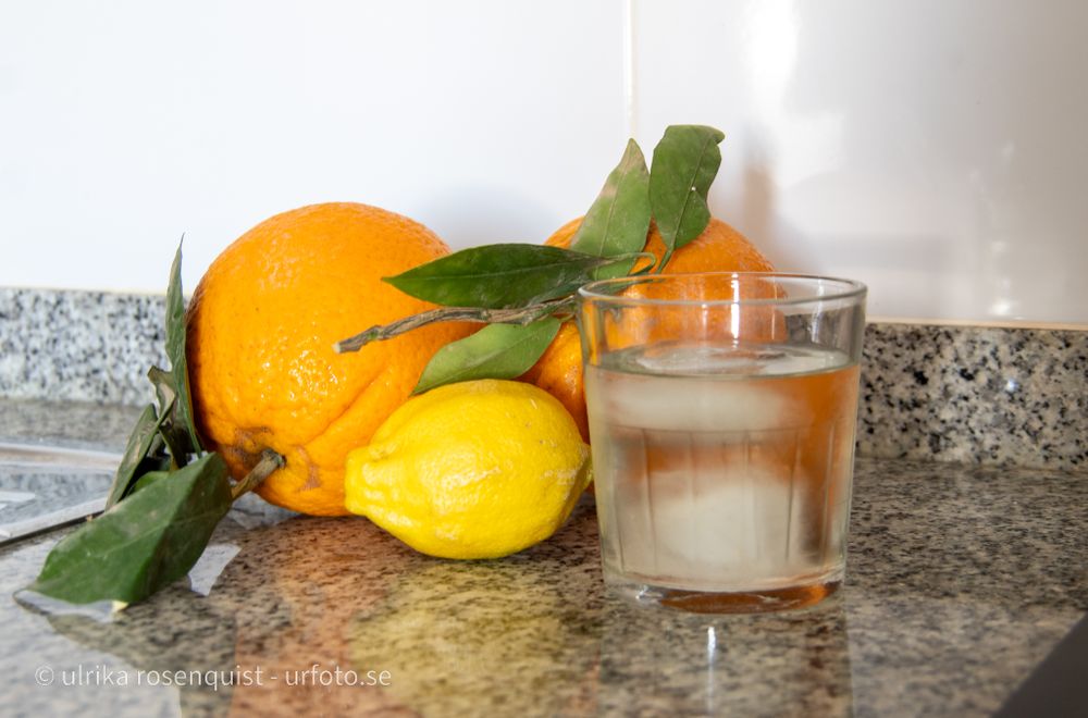 Fresh citrus fruits and a glass of iced beverage on granite countertop with green leaves.