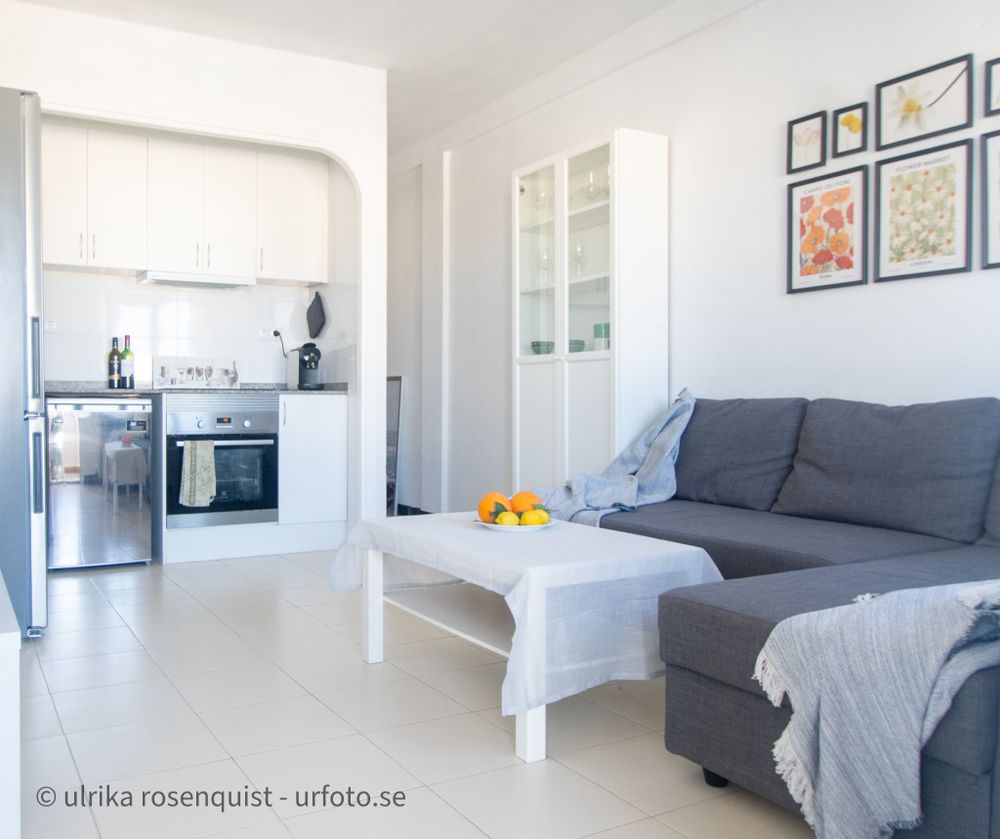Clean white modern apartment interior with grey sofa, open kitchen and minimalist decor.