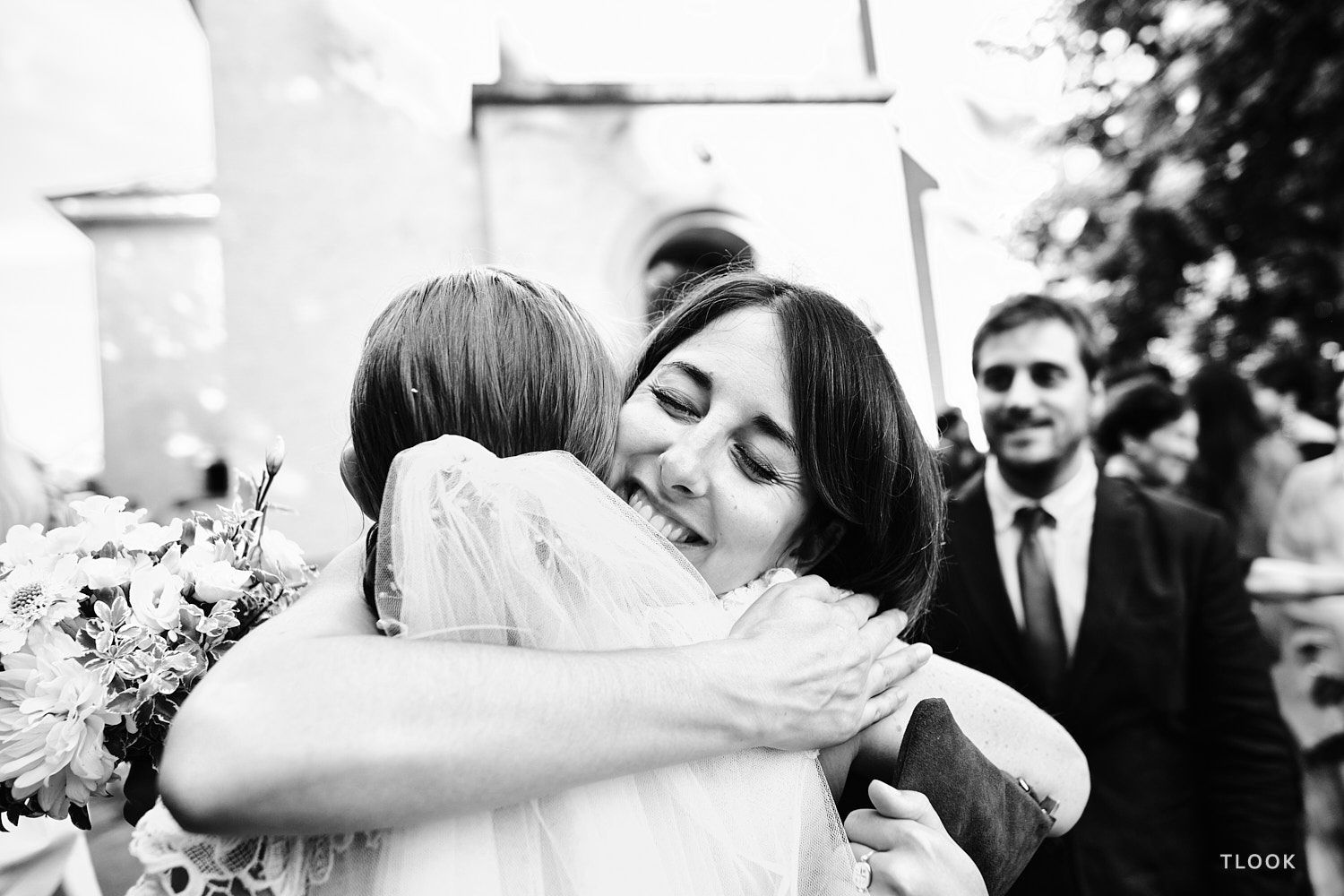 TLOOK photographe de mariage de style documentaire, une amie embrasse la mariée à la sortie de l'église