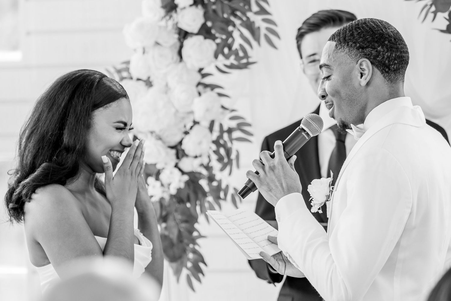 Black and white photo of groom reading heartfelt vows to emotional bride at wedding ceremony.