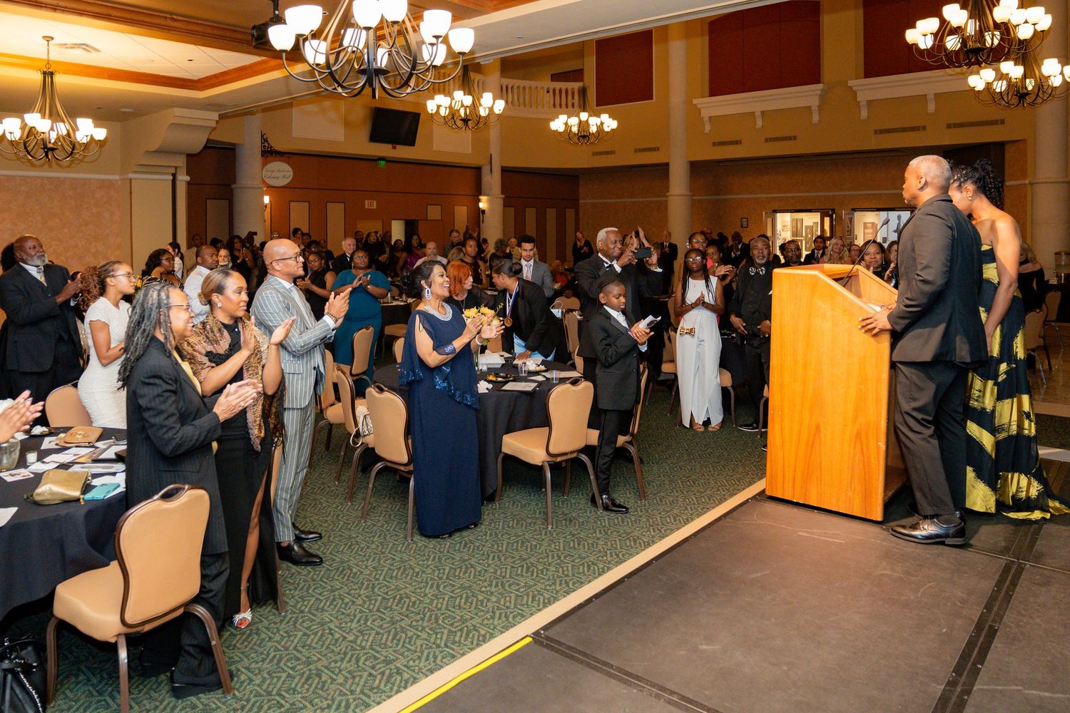 Audience members applauding during a presentation in an elegant ballroom setting.