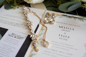 Wedding invitation with delicate floral designs and jewelry details on white paper.