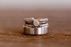Close-up of elegant diamond wedding rings and matching silver band on wooden surface.