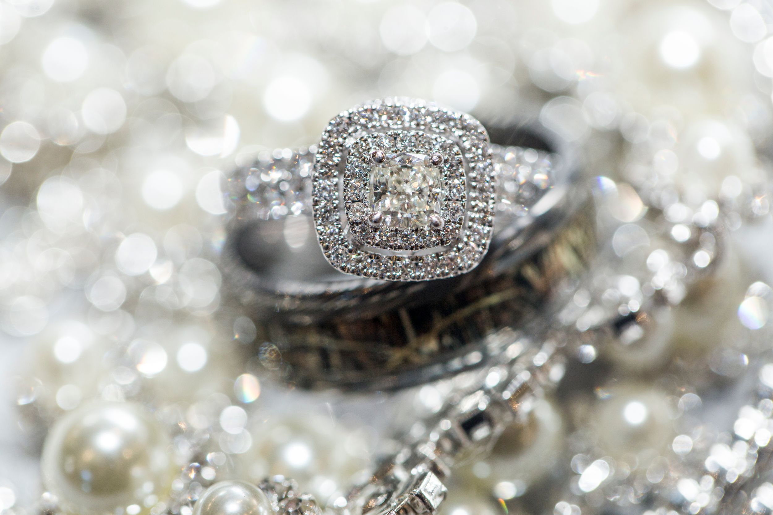 Diamond engagement ring and wedding bands photographed with bokeh and pearl details.