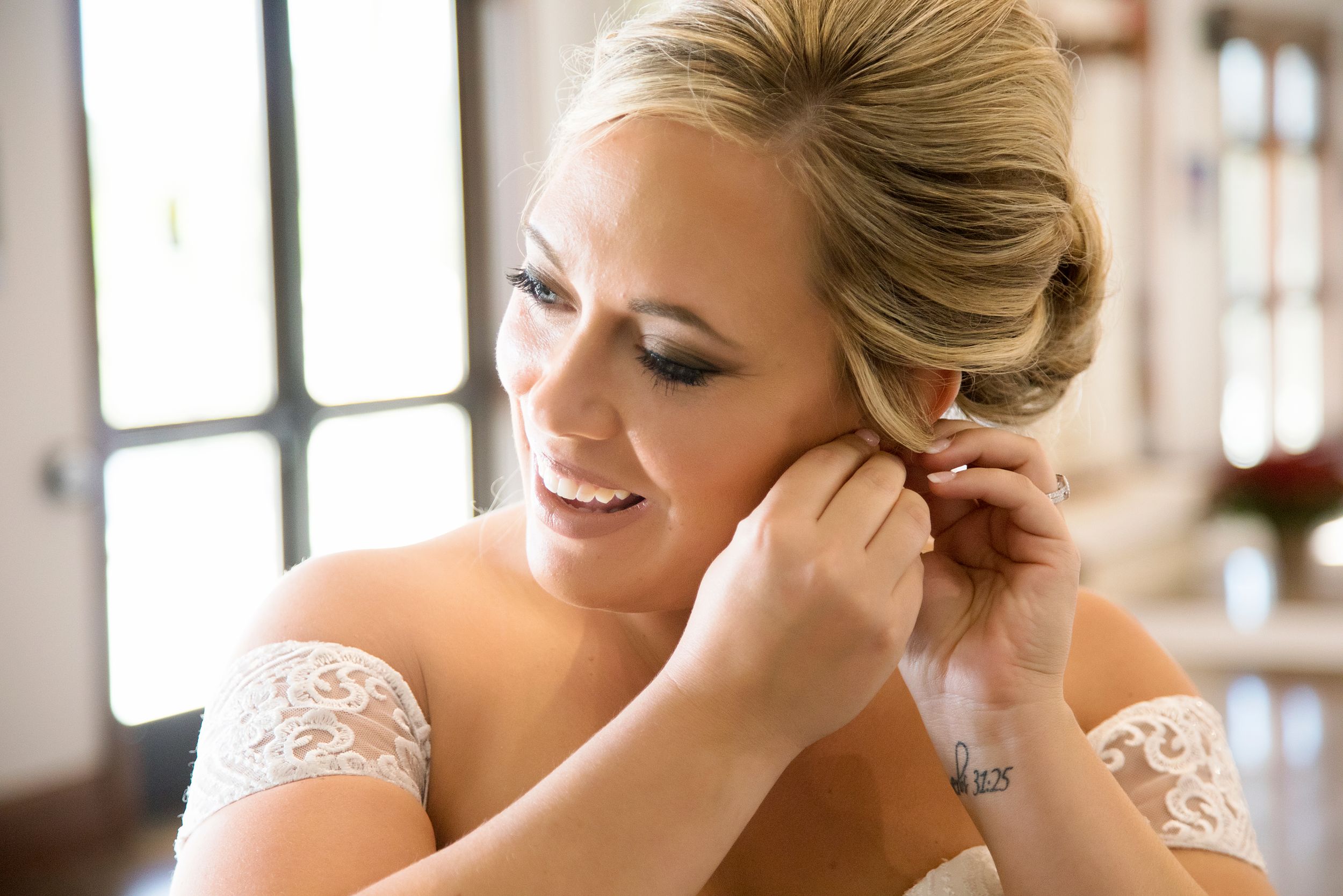 A close-up view of delicate lace details and elegant earrings being put on during wedding preparations.