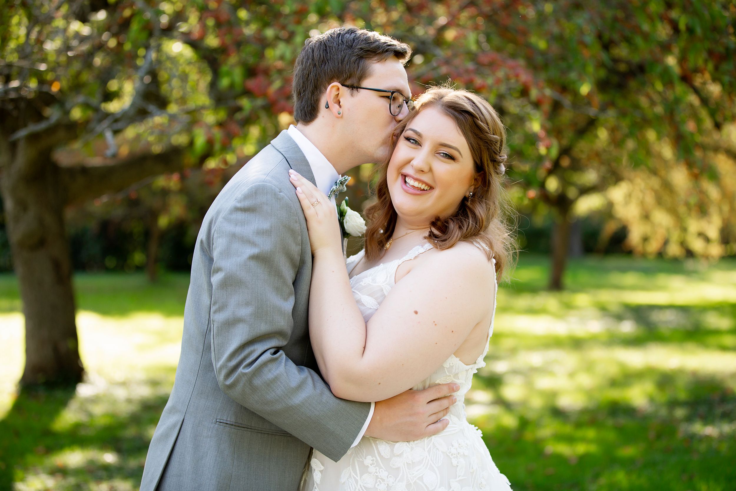 A joyful wedding couple embraces in a sunny garden setting.