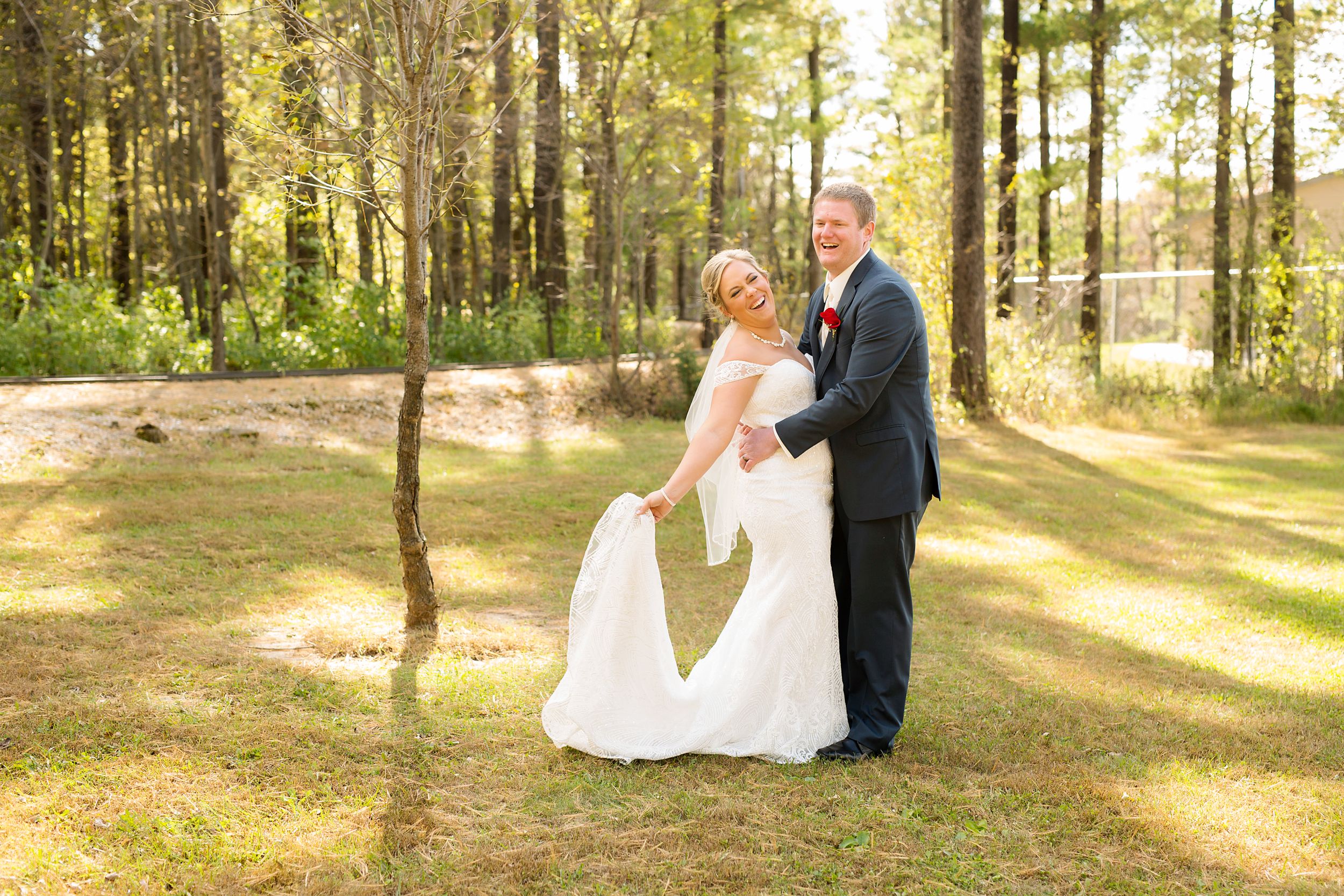 A romantic wedding portrait in a sunny wooded area with golden sunlight filtering through the trees.