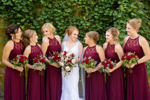 Wedding party in burgundy dresses holding vibrant bouquets against a leafy green backdrop.